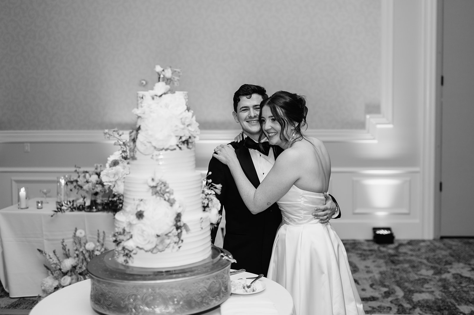 Black and white photo of a bride and groom smiling after cutting into their wedding cake