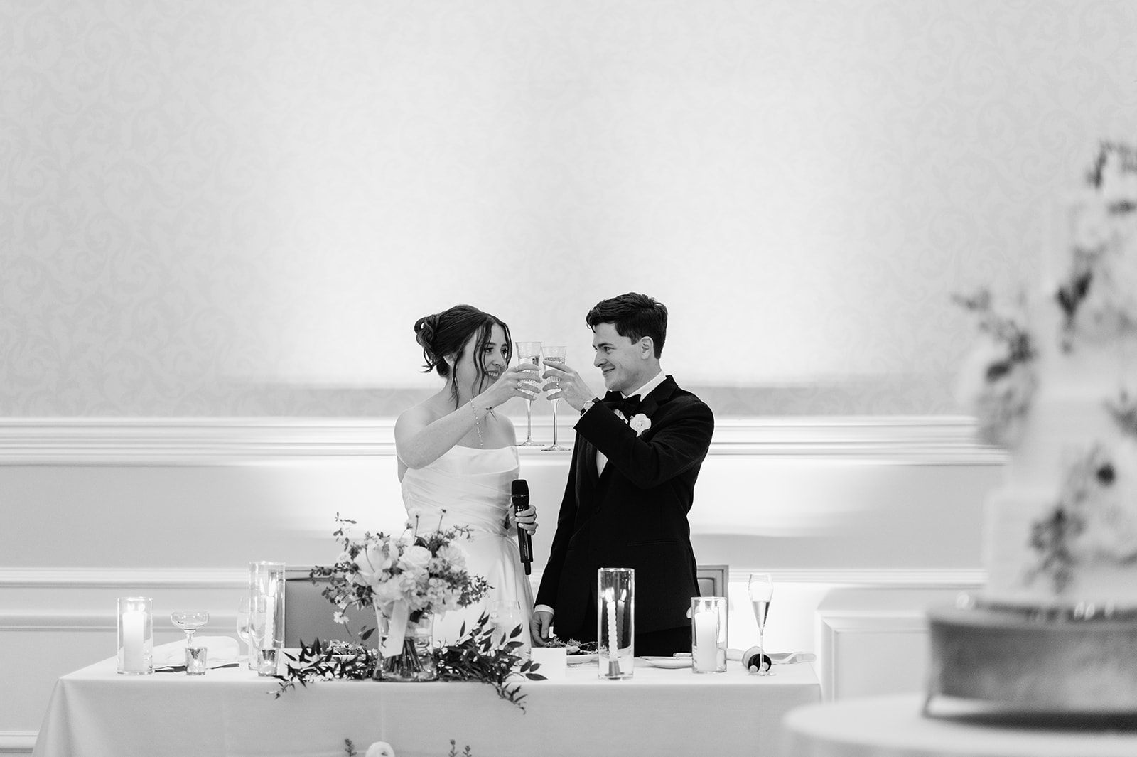 Black and white photo of a bride and groom toasting glasses after their speech