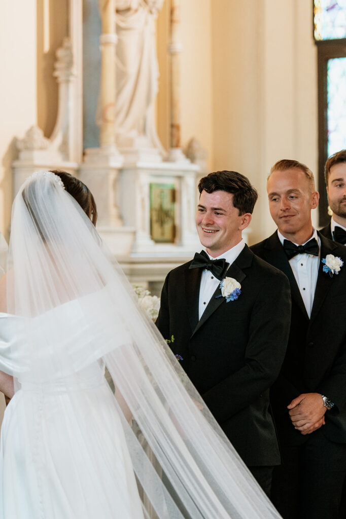 Groom smiles as he sees his bride for the first time during their Notre Dame wedding ceremony.