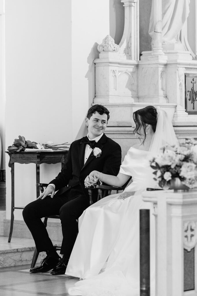 Black and white photo of a bride and groom sitting and holding hands during their Catholic Notre Dame wedding ceremony