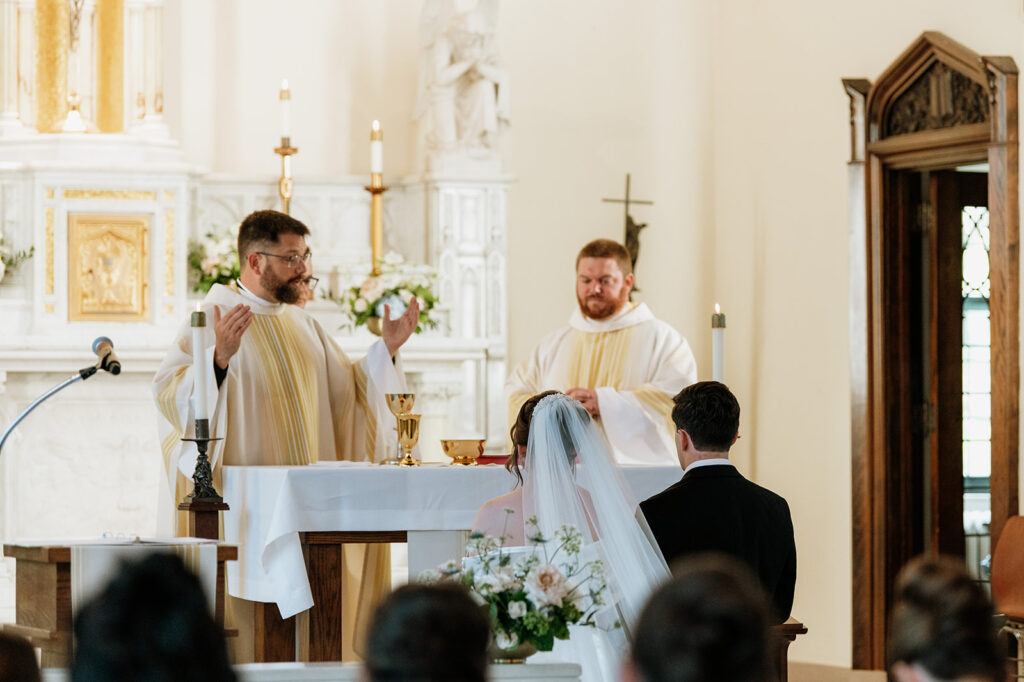 Bride and groom kneel at the altar while priests lead the sacrament of marriage.