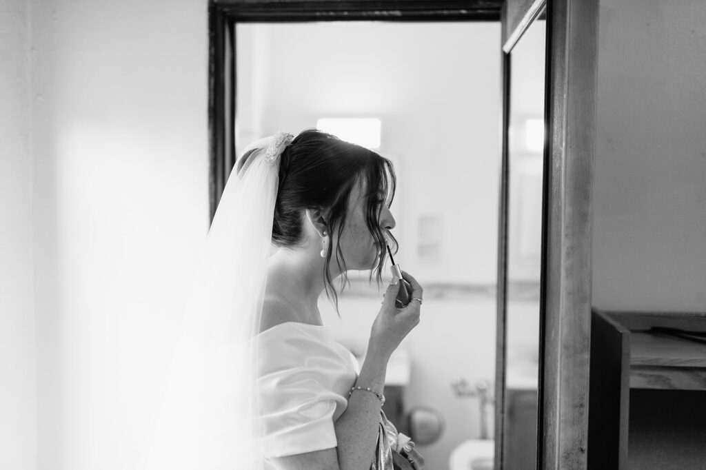 Candid black and white photo of a bride touching up her lipstick before her ceremony