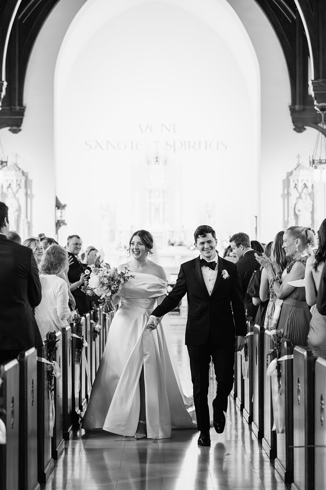 Black and white photo of a bride and groom walking back down the aisle after their Notre Dame wedding ceremony at The Holy Spirit Chapel