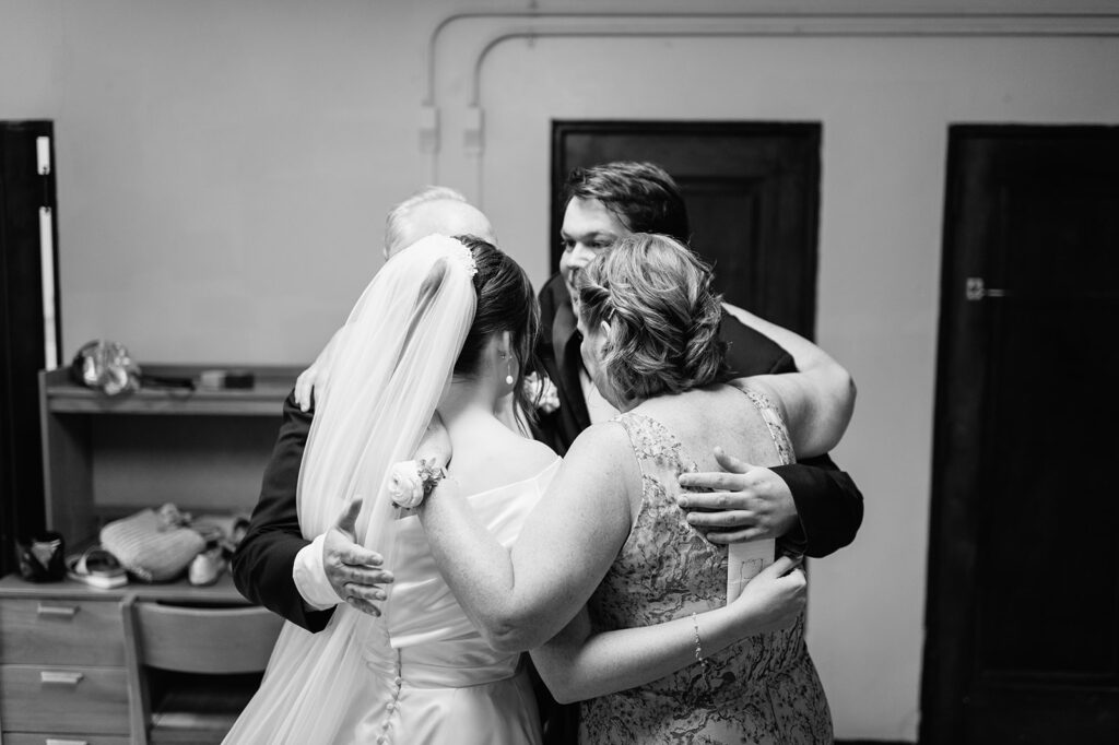 Candid black and white photo of a bride hugging a few close family members before her ceremony