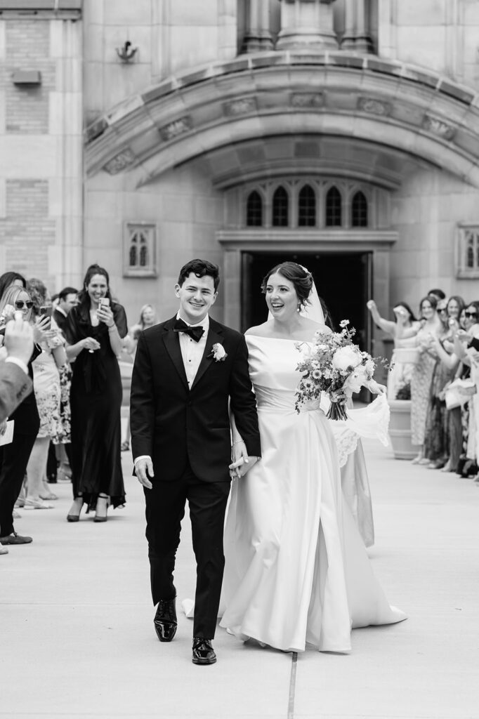 Candid black and white photo of a bride and groom holding hands and walking out of the church as husband and wife
