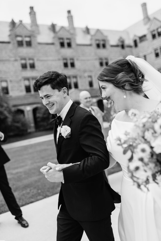 Candid black and white photo of a bride and groom holding hands and walking out of the church as husband and wife