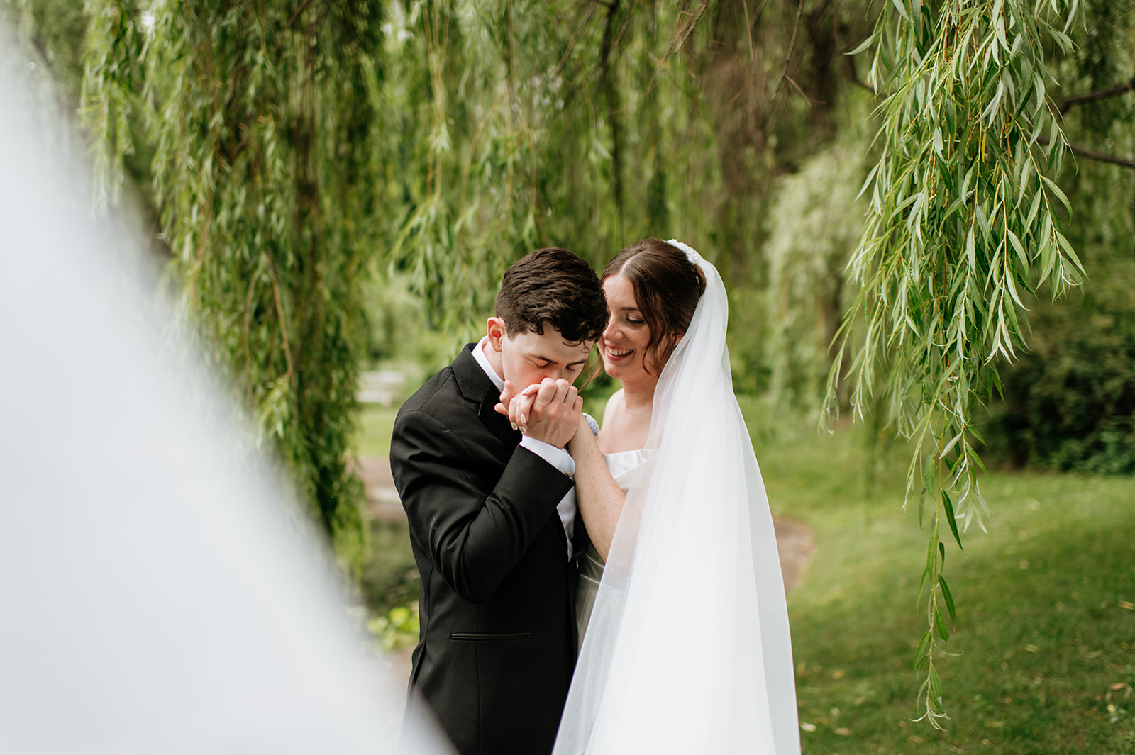 Wide shot of a groom kissing his brides hand during their outdoor Notre Dame wedding portraits