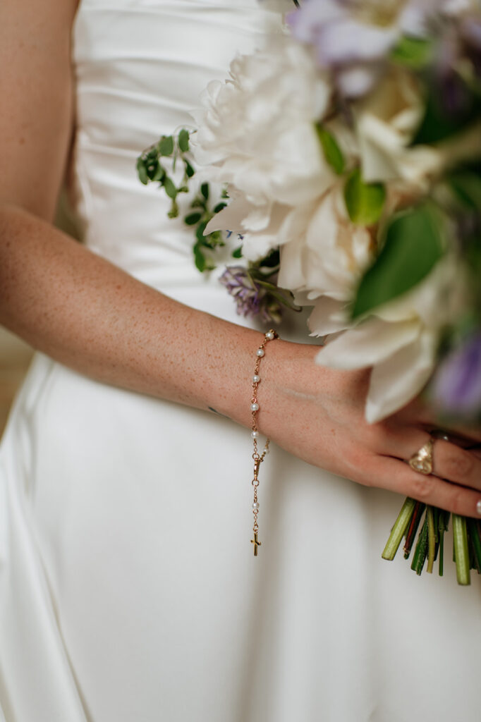 Close up shot of a bride holding her bouquet of ivory and purple flowers.