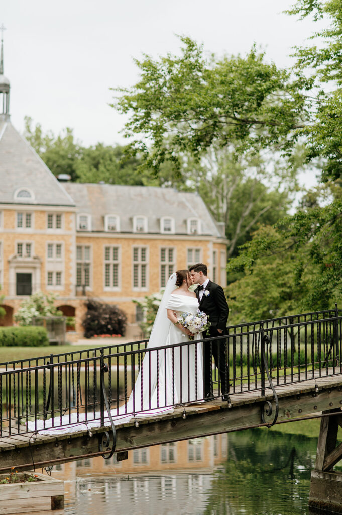 Bride and groom kiss on a small bridge with Saint Mary’s College building in the background.