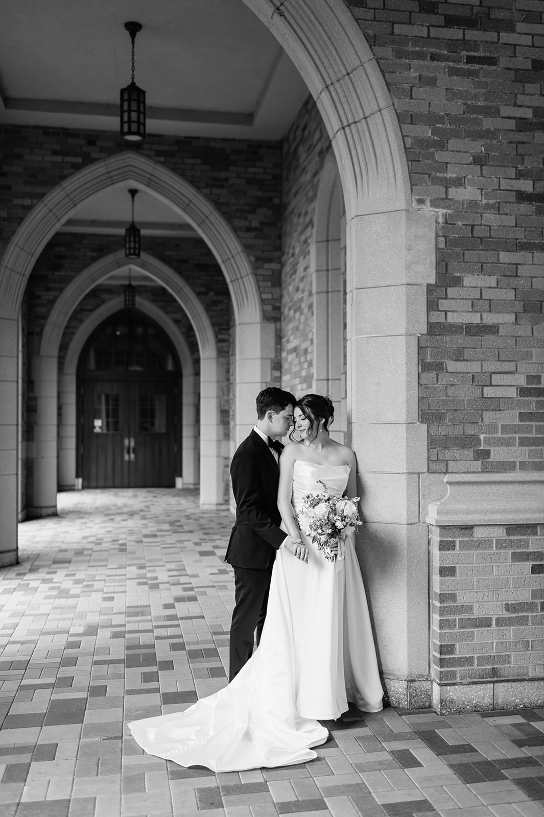 Black and white portrait of bride and groom standing together in the arched walkways their Notre Dame wedding portraits.