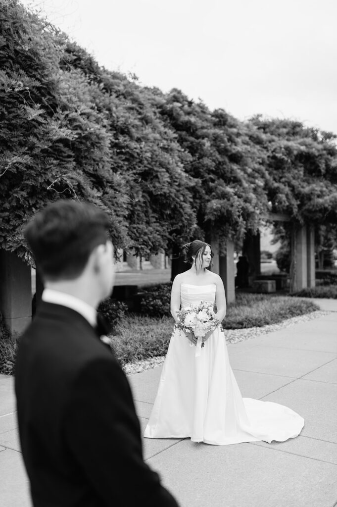 Editorial black and white photo of a groom admiring his bride from afar during their Notre Dame wedding portraits.