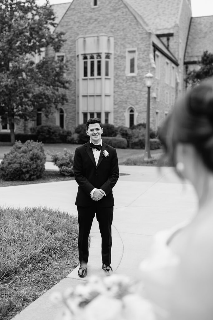 Editorial black and white photo of a groom admiring his bride from afar during their Notre Dame wedding portraits.