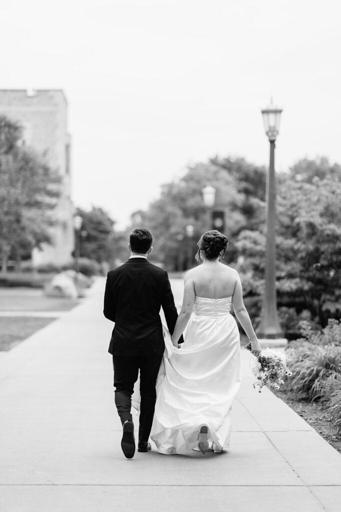 Black and white photo of a bride and groom walking on the campus of Notre Dame