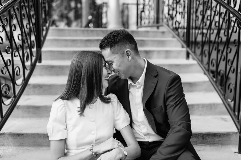 Black and white photo of a couple sitting and touching noses on the staircase outside LaFortune during their University of Notre Dame engagement photos.
