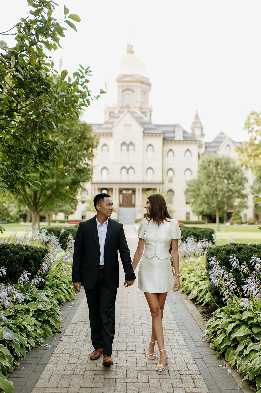 Couple walking hand in hand with the Main Building and golden dome in the background.