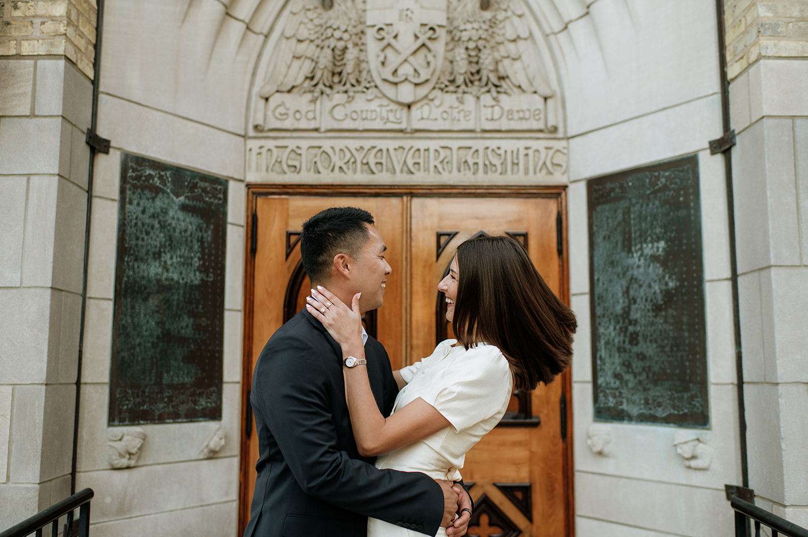 Couple laughing together outside the Basilica of the Sacred Heart with the “God, Country, Notre Dame” doors behind them.