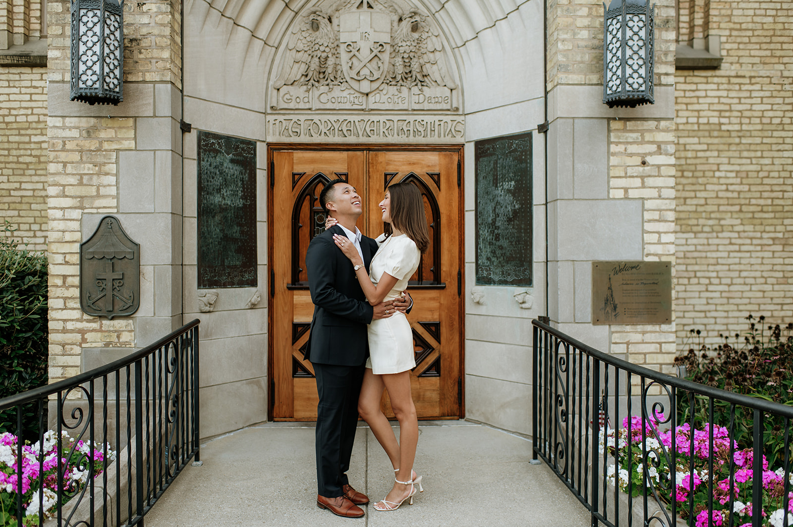 Couple smiling together outside the Basilica of the Sacred Heart with the “God, Country, Notre Dame” doors behind them.