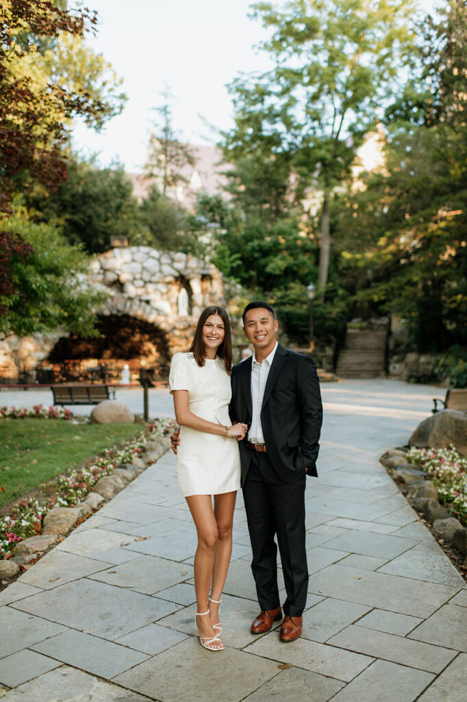 Couple standing near the stone grotto surrounded by greenery during evening portraits.