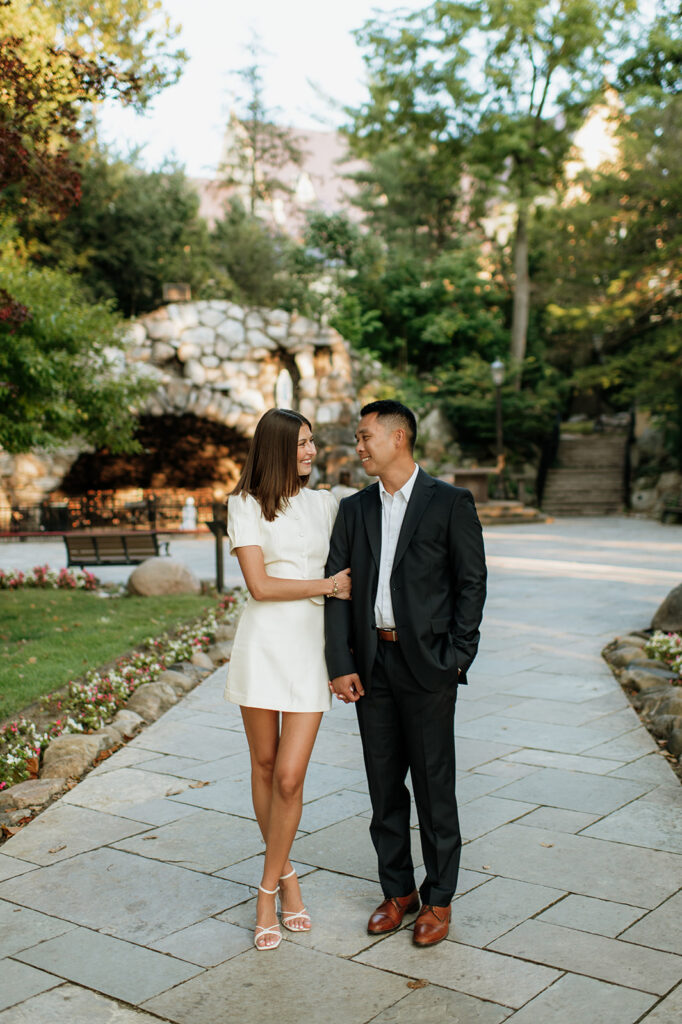 Couple smiling at each other near the stone grotto surrounded by greenery during evening portraits.