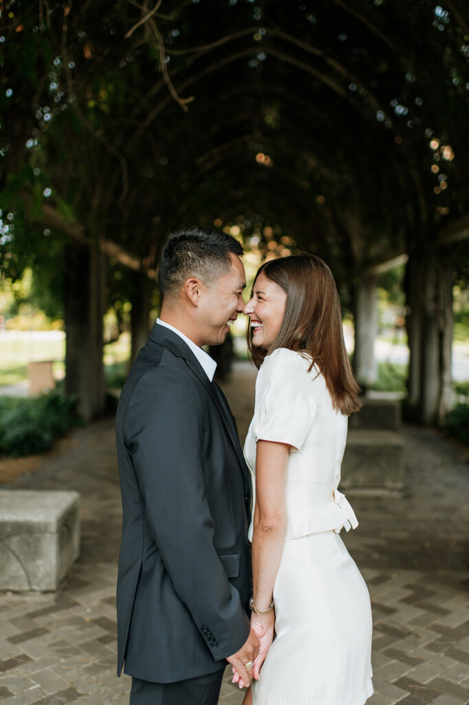 Couple laughing beneath the vine-covered walkway during elegant University of Notre Dame engagement photos.