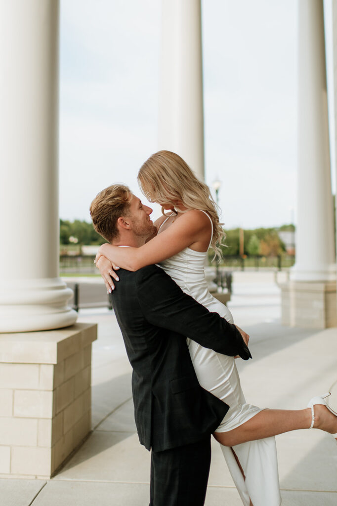 Man lifting his fiancé near the grand pillars of the Elkhart County Courthouse