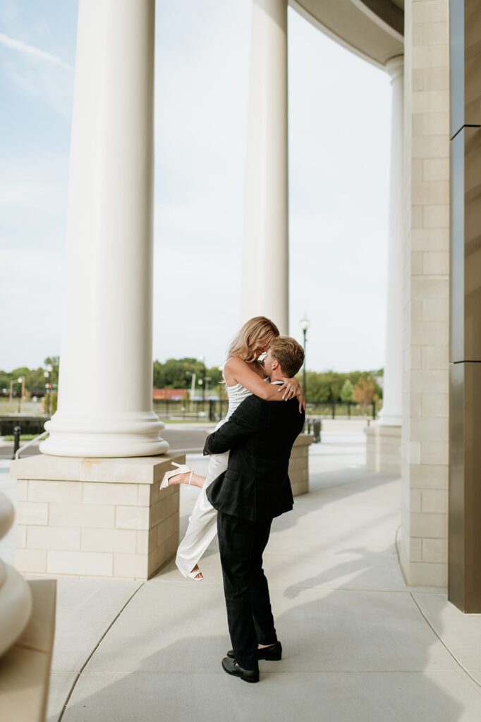 Man lifting his fiancé near the grand pillars of the Elkhart County Courthouse