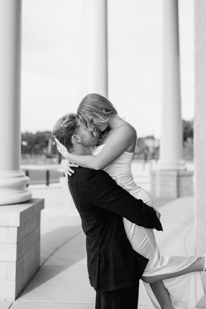 Black and white photo of a man lifting his fiancé near the grand pillars of the Elkhart County Courthouse