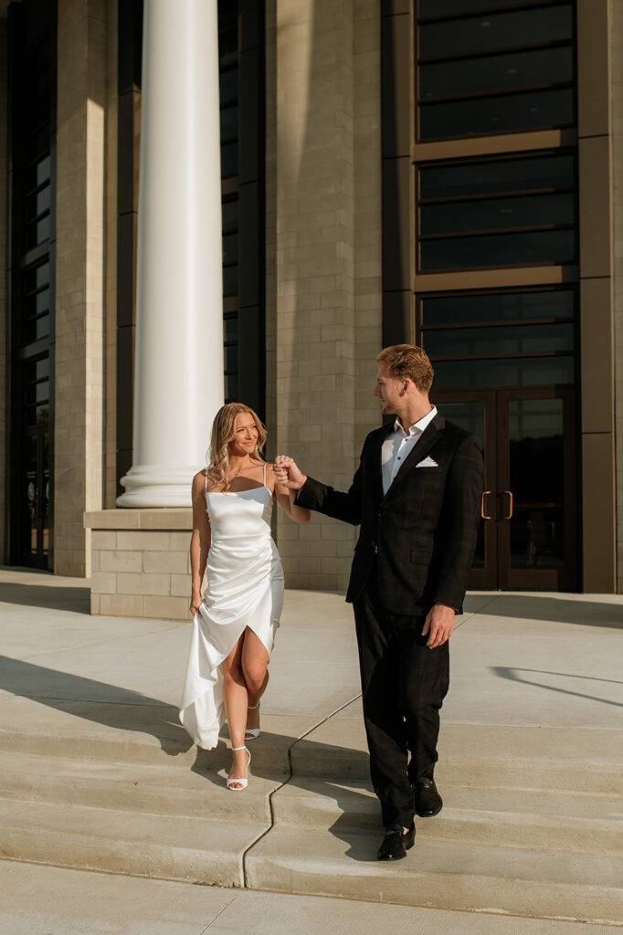 Couple walking down courthouse steps hand in hand, bathed in golden light