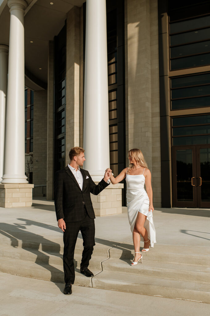 Couple walking down courthouse steps hand in hand, bathed in golden light