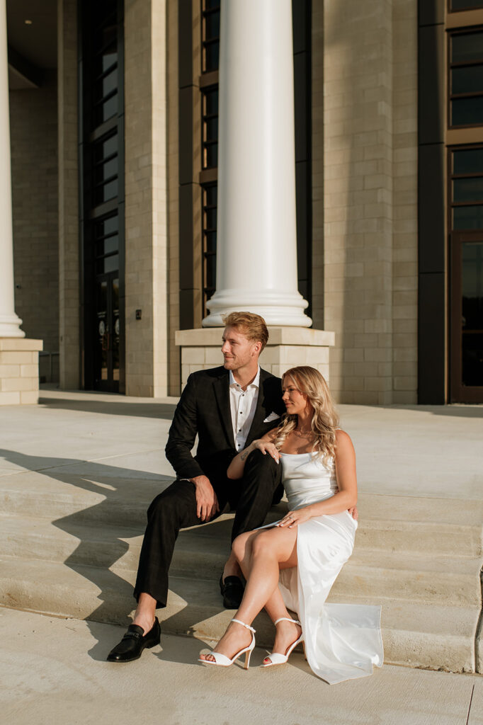 Couple sitting on the courthouse steps in elegant outfits for their Goshen, Indiana engagement photos