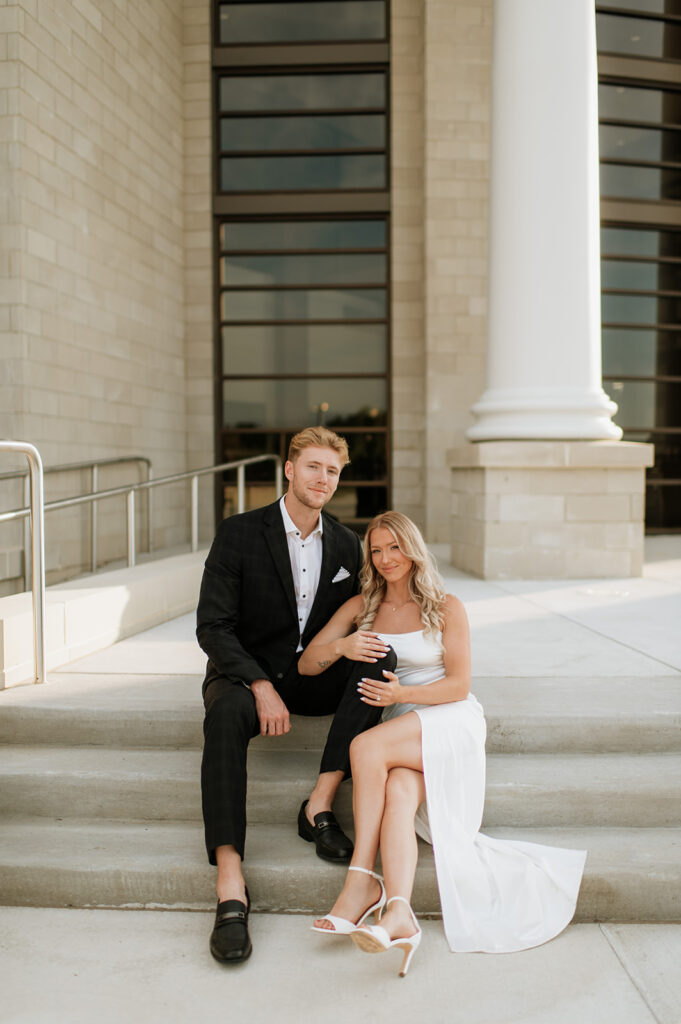 Couple sitting on the courthouse steps in elegant outfits for their Goshen, Indiana engagement photos