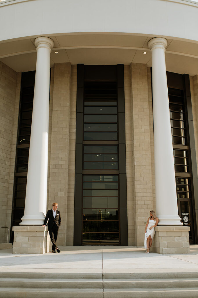 Wide photo showing the grand architecture of the Elkhart County Courthouse with the couple standing by opposite pillars