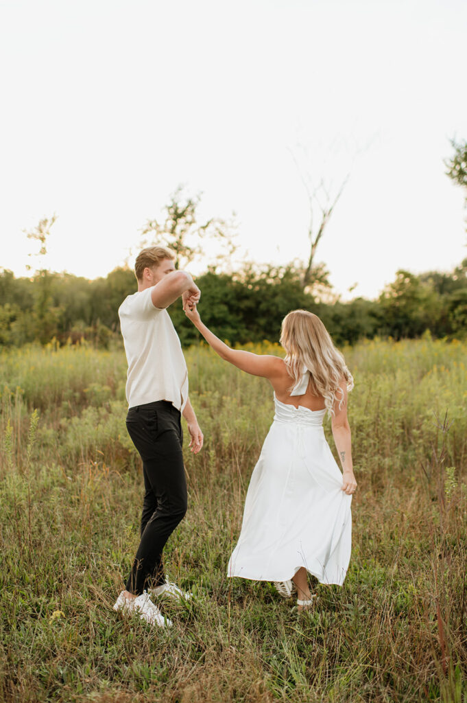 Couple spinning each other in the tall grass at golden hour