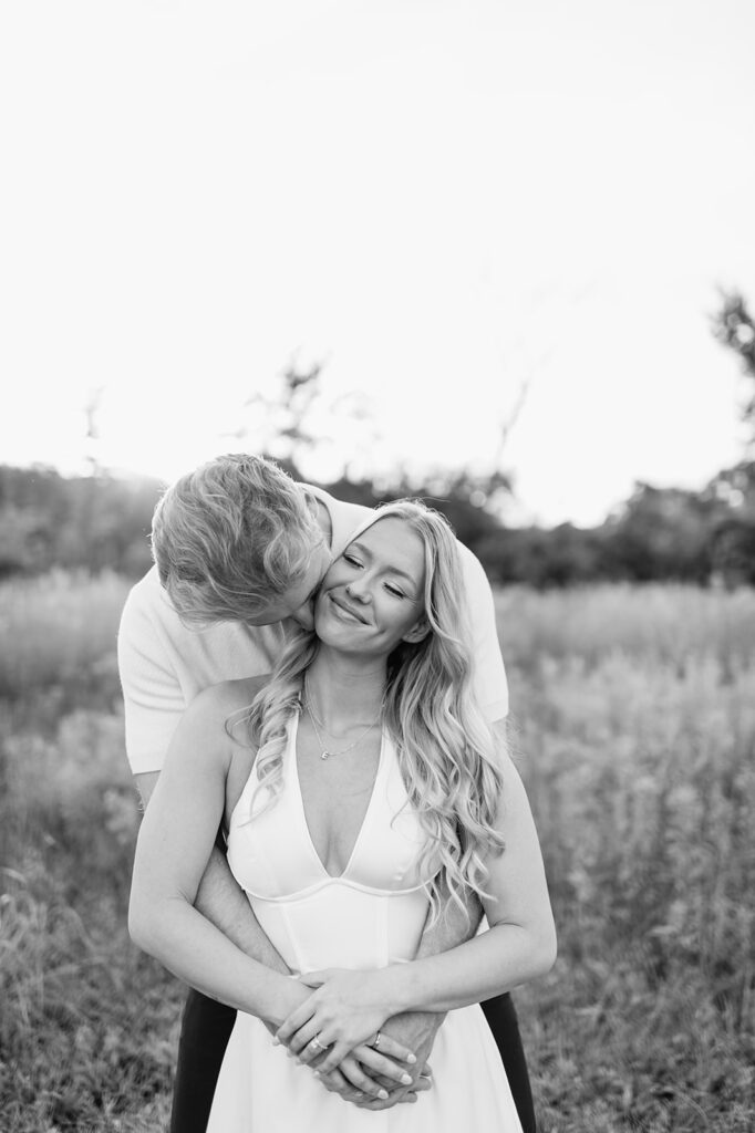 Black and white photo of a man kissing his fiancés neck during their field engagement session