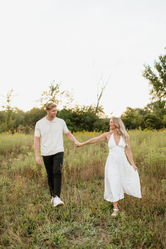 Couple walking hand in hand through the grass with warm evening light