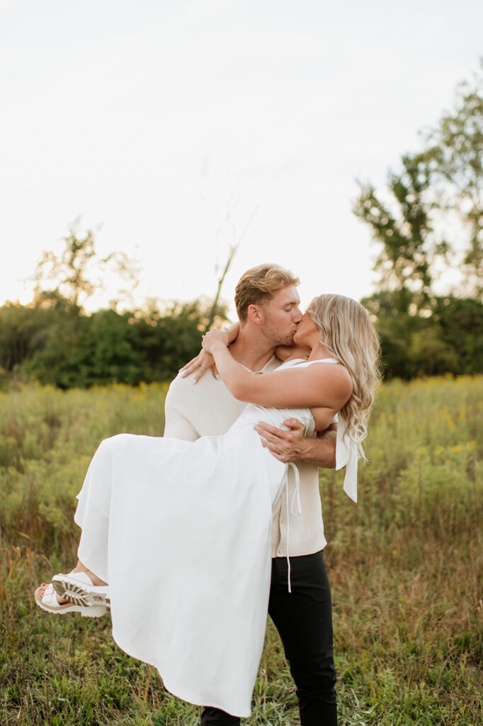 Man carrying his fiancé during their field engagement photos in Goshen, Indiana