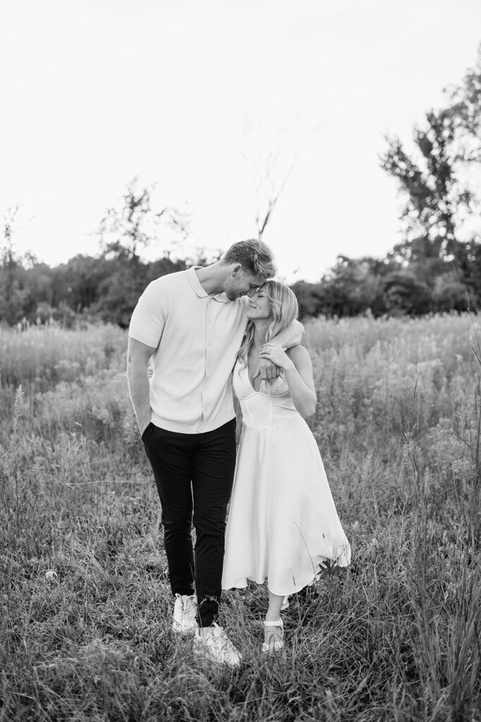 Black and white photo of a couple touching noses as they pose in an open field for their Goshen, Indiana engagement photos