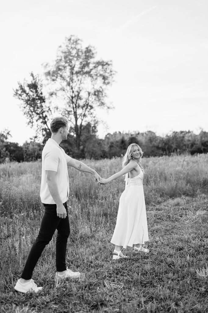 Black and white photo of a couple walking through a field hand in hand