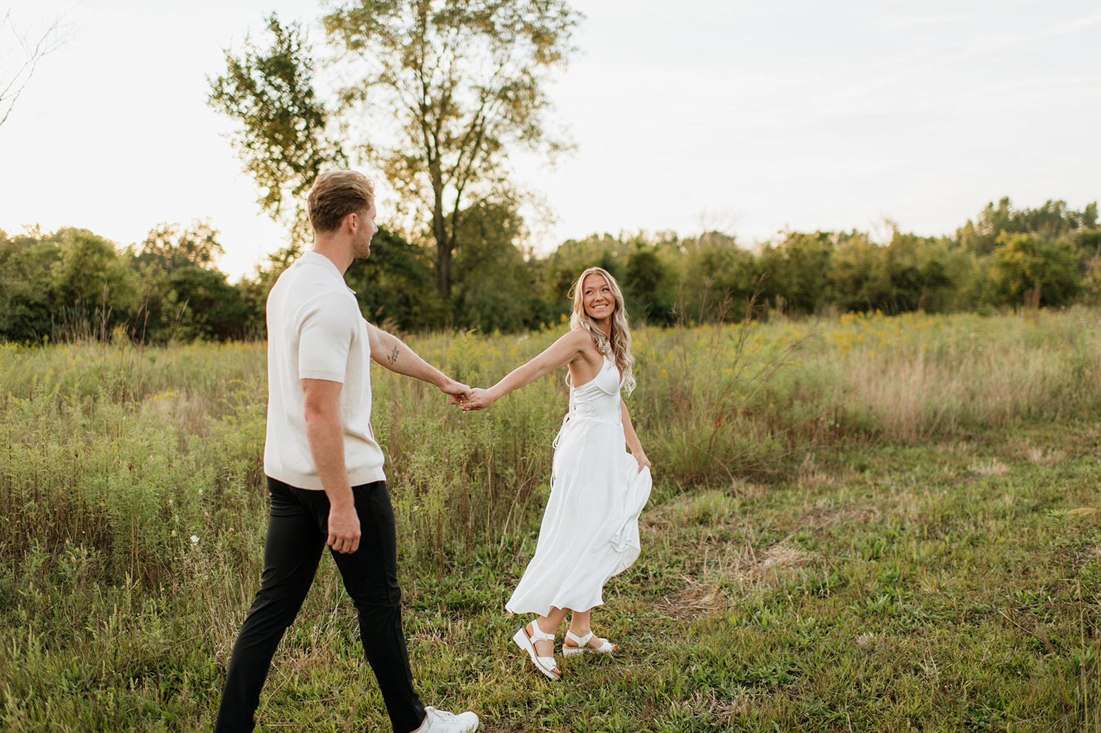 Couple walking hand in hand through a field 