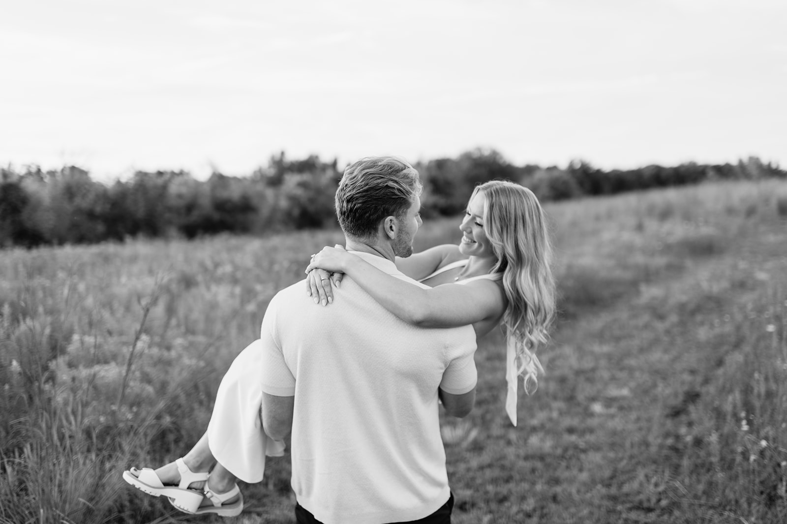 Black and white photo of a man carrying his fiancé through a field in Goshen, Indiana