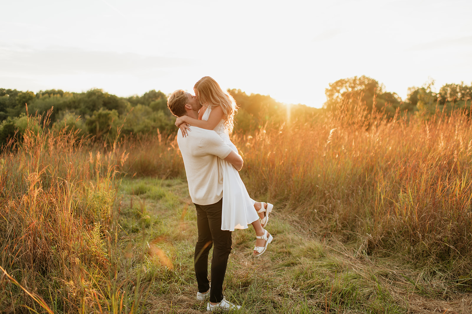 Man lifting and kissing his fiancé during their golden hour field engagement photos in Goshen, Indiana