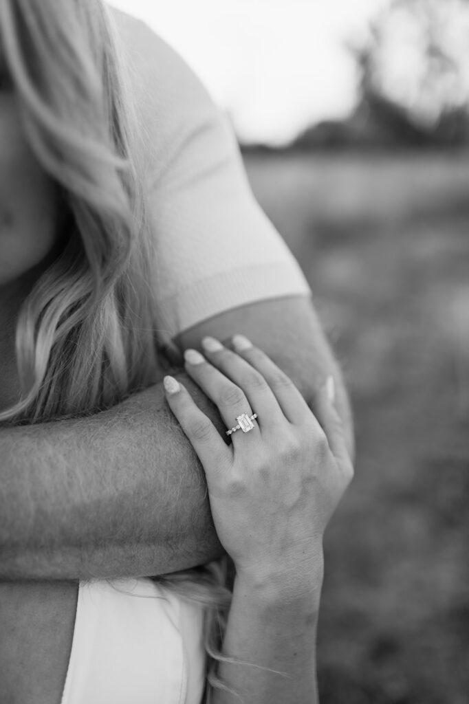 Black and white close up shot of a woman holding her fiancés arm and showing off her engagement ring