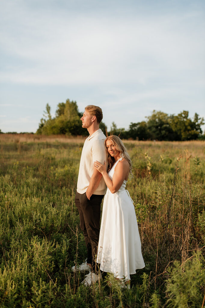 Couple standing in tall grass with warm sunlight shining across the field