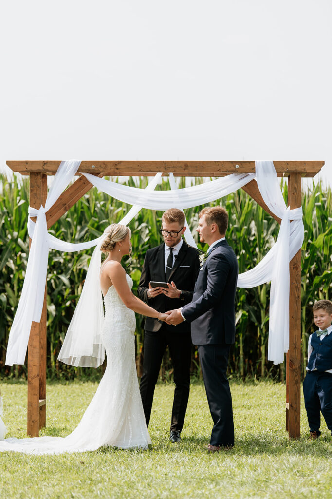 Couple holding hands under ceremony arch with cornfield backdrop at Rock Run Creek Barn.
