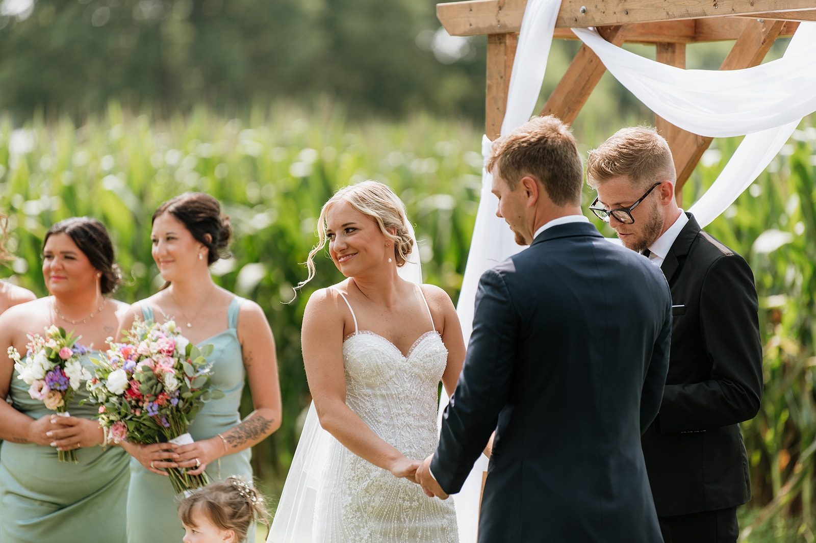 Bride smiling during vows with bridesmaids in mint dresses beside her at Rock Run Creek Barn.