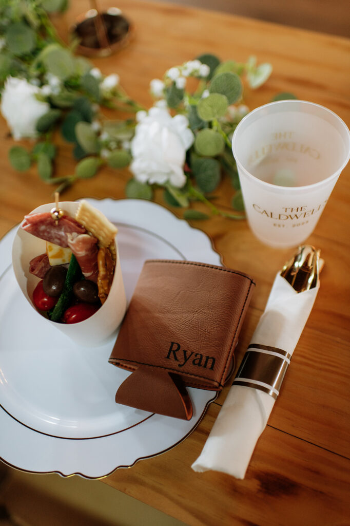 Personalized place setting with custom koozie, charcuterie cup, and name cup for guests at Rock Run Creek Barn wedding reception.