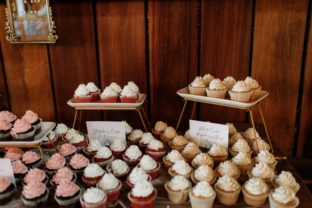 Strawberry and white cupcakes with buttercream frosting displayed on dessert table at Rock Run Creek Barn wedding reception.