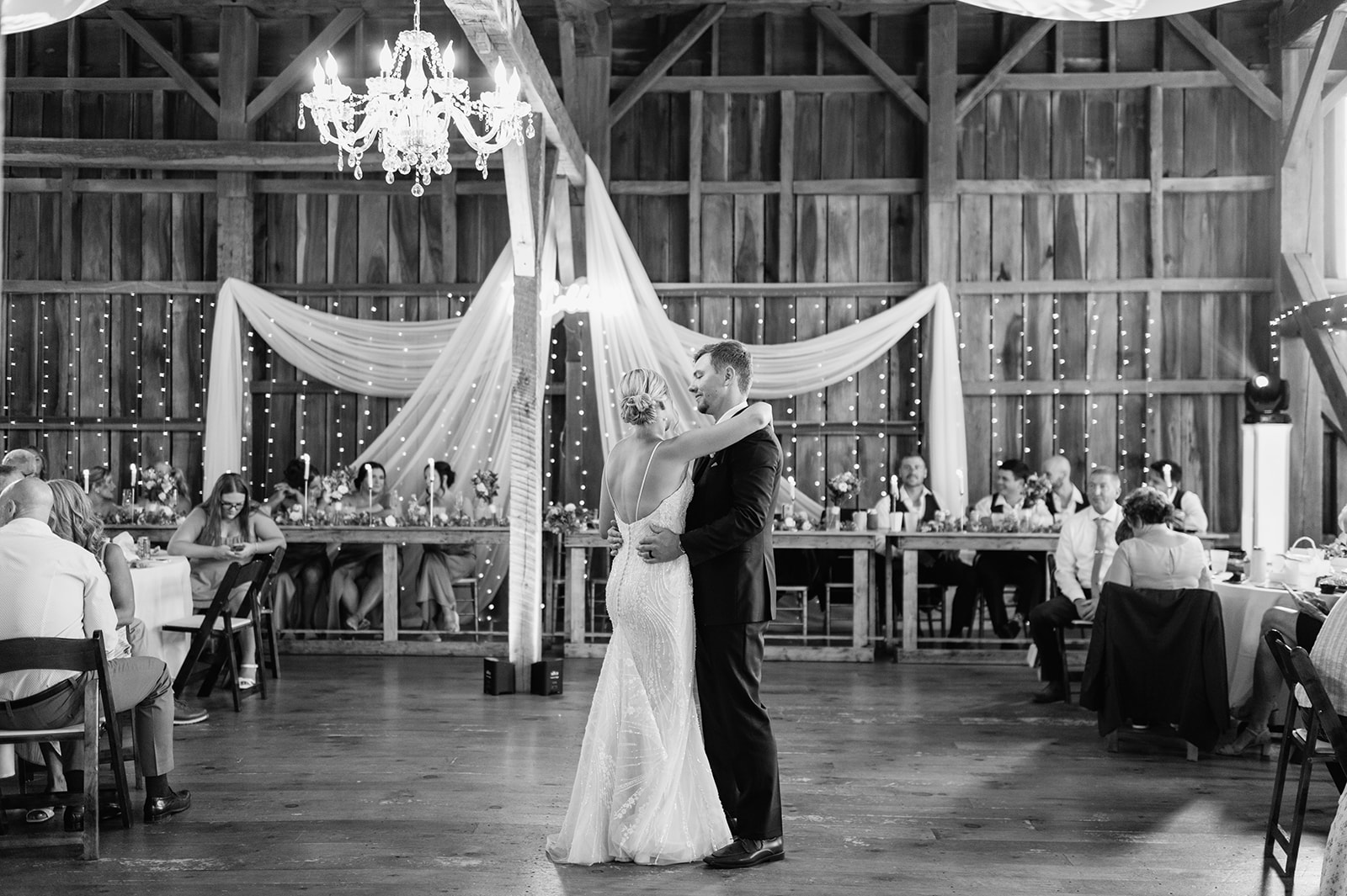Bride and groom sharing first dance under chandelier and twinkle lights inside The Event Barn at Rock Run Creek Barn.