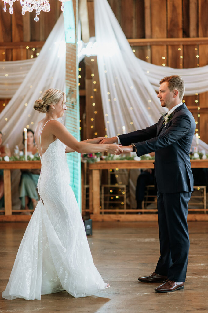 Bride and groom holding hands during first dance inside Rock Run Creek Barn reception space.