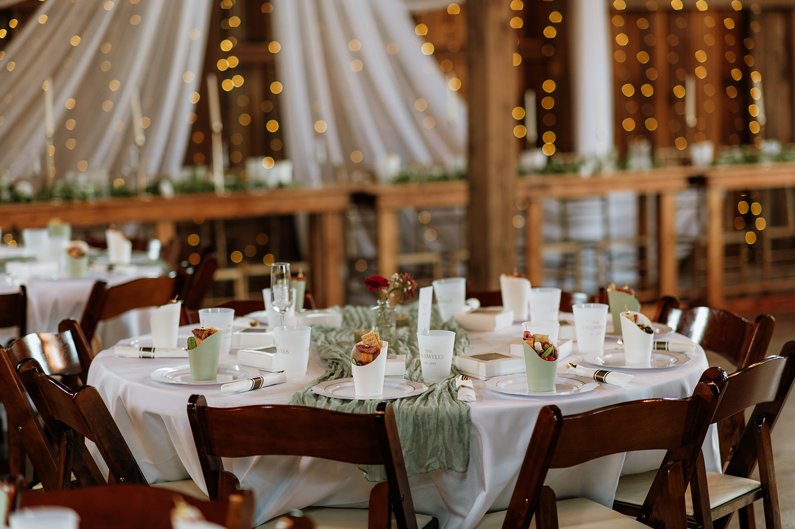 Wedding reception tables decorated with white linens, greenery runners, and candles at Rock Run Creek Barn in Goshen, Indiana.